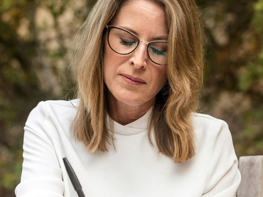 Woman with glasses writing notes, reflecting on executive function strategies for neurodivergent adults, emphasizing personal and professional development.